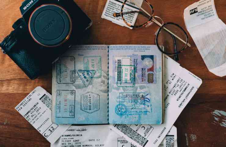 Foto di un passaporto aperto con intorno una macchina fotografica e degli occhiali